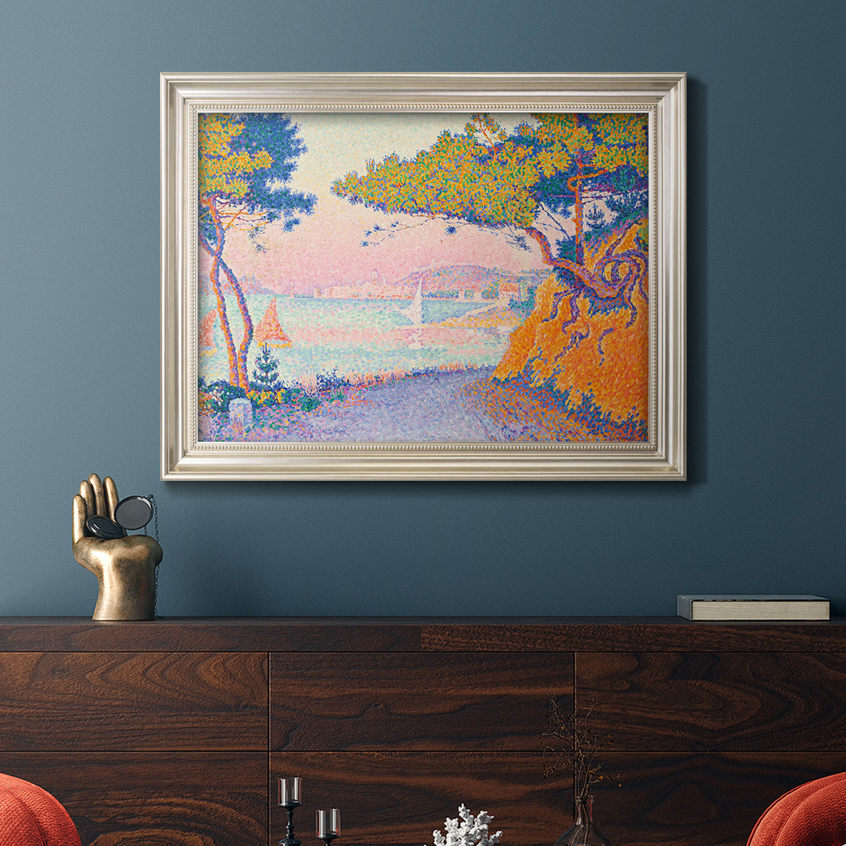 Pointillist coastal seascape by Paul Signac in an ornate champagne frame displayed in a dark-toned interior setting.