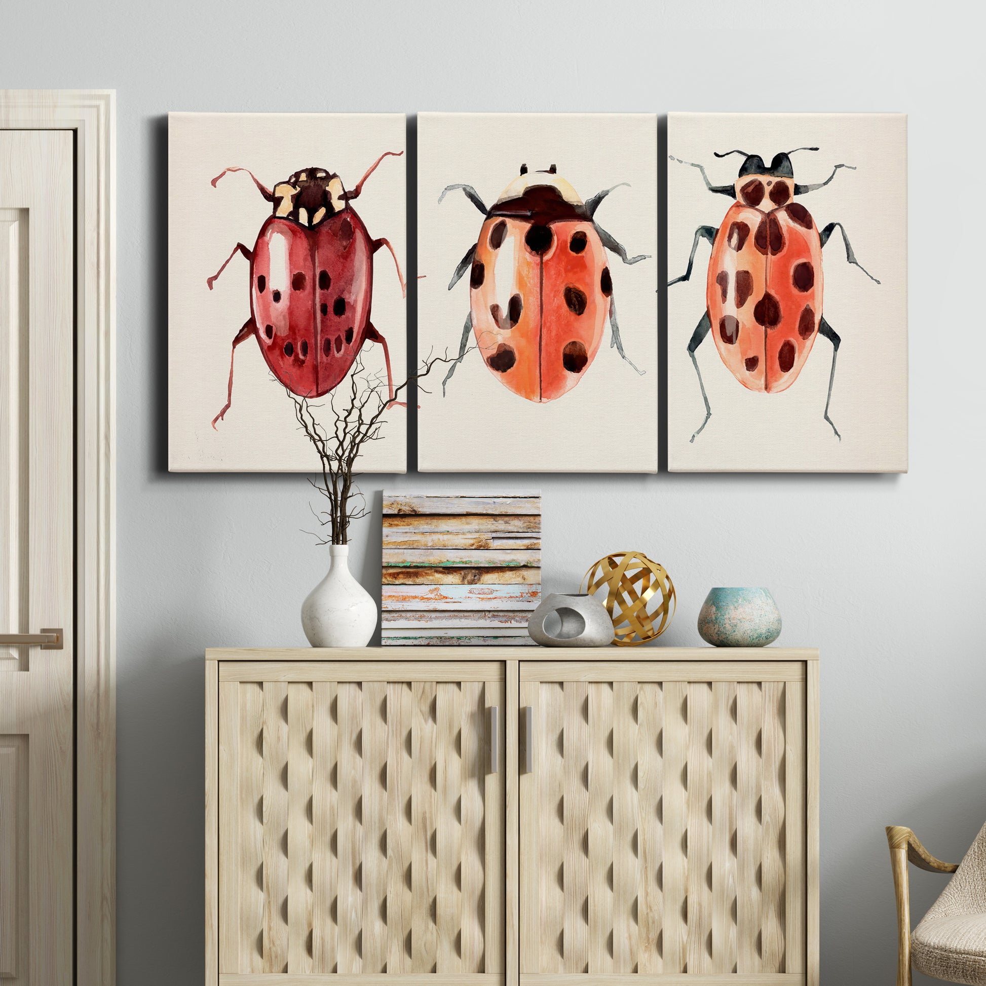 Three-panel canvas wall art featuring ladybugs on green foliage, displayed above a cabinet in an entryway.