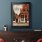 Realist city street scene by Johannes Vermeer in an ornate black frame with gilded inner detail displayed in a dark-toned interior setting.