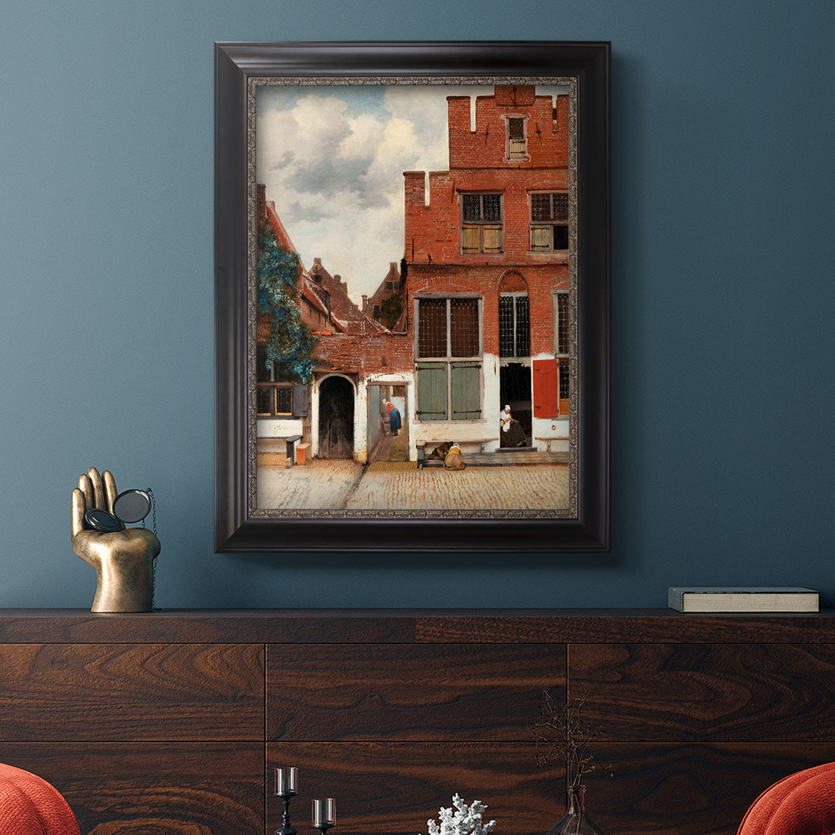Realist city street scene by Johannes Vermeer in an ornate black frame with gilded inner detail displayed in a dark-toned interior setting.
