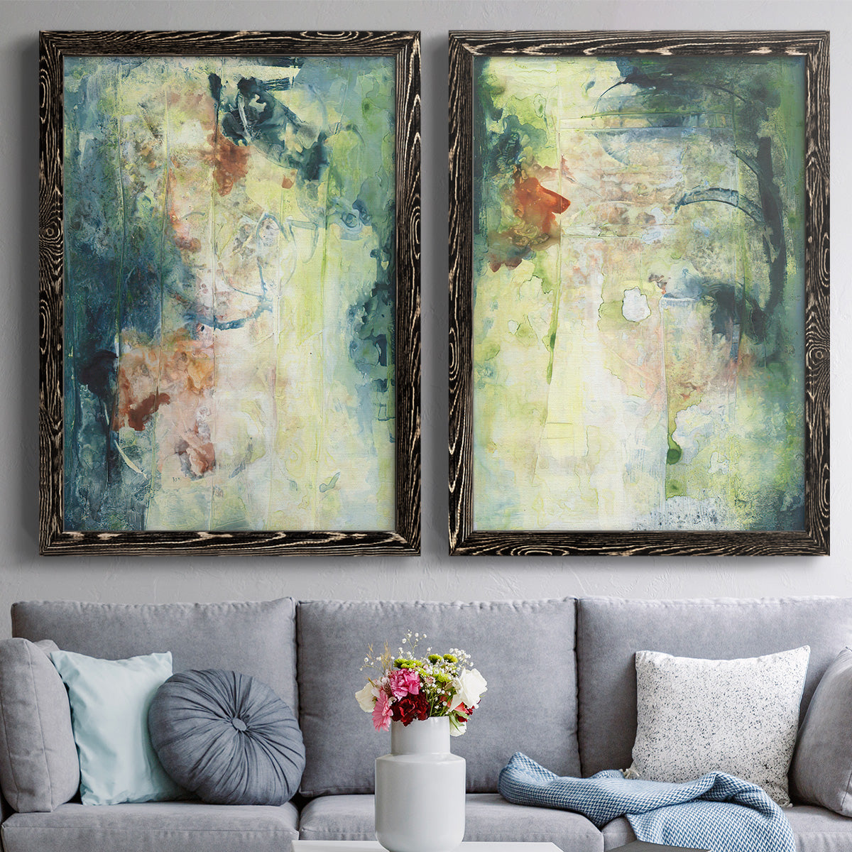 Set of two black barnwood framed canvas prints depicting paired nature-inspired mixed-media abstracts with vertical organic marks, pale light passages, and weathered surfaces above a sofa in a contemporary living room.