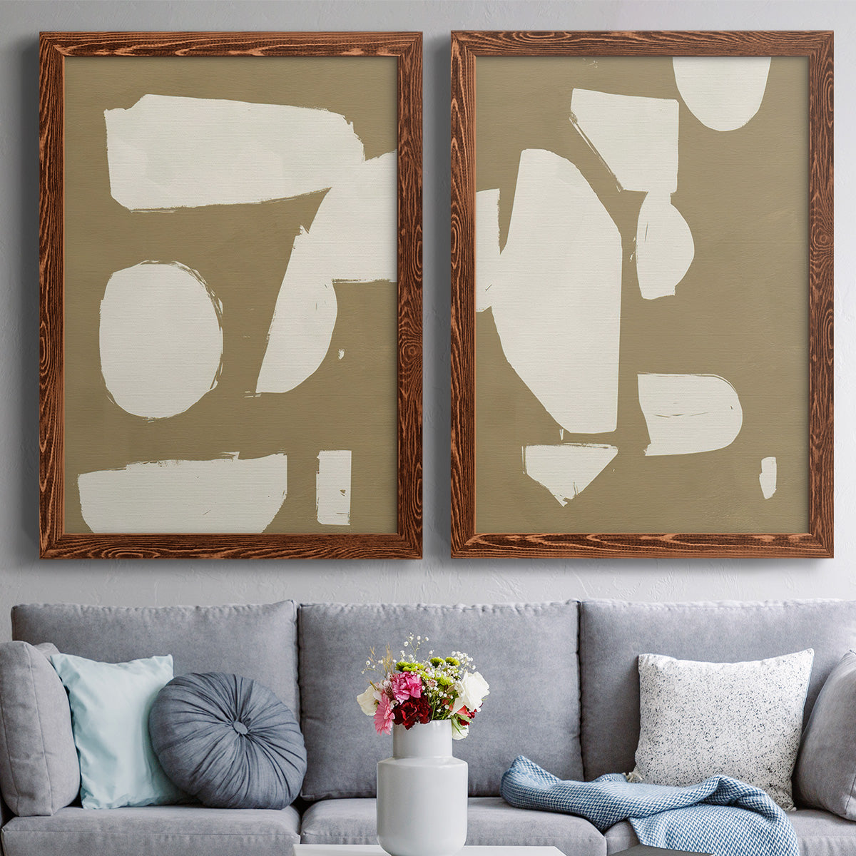 Set of two maple barnwood framed canvas prints depicting paired bold minimalist shape abstracts with flat blocky forms, rough painted edges, and strong negative space above a sofa in a contemporary living room.