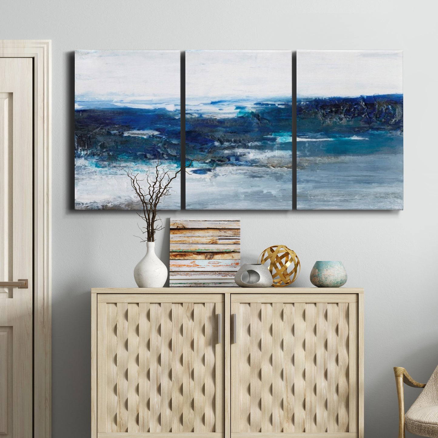Three-panel canvas wall art featuring moody abstract sea with depth, displayed above a cabinet in an entryway.