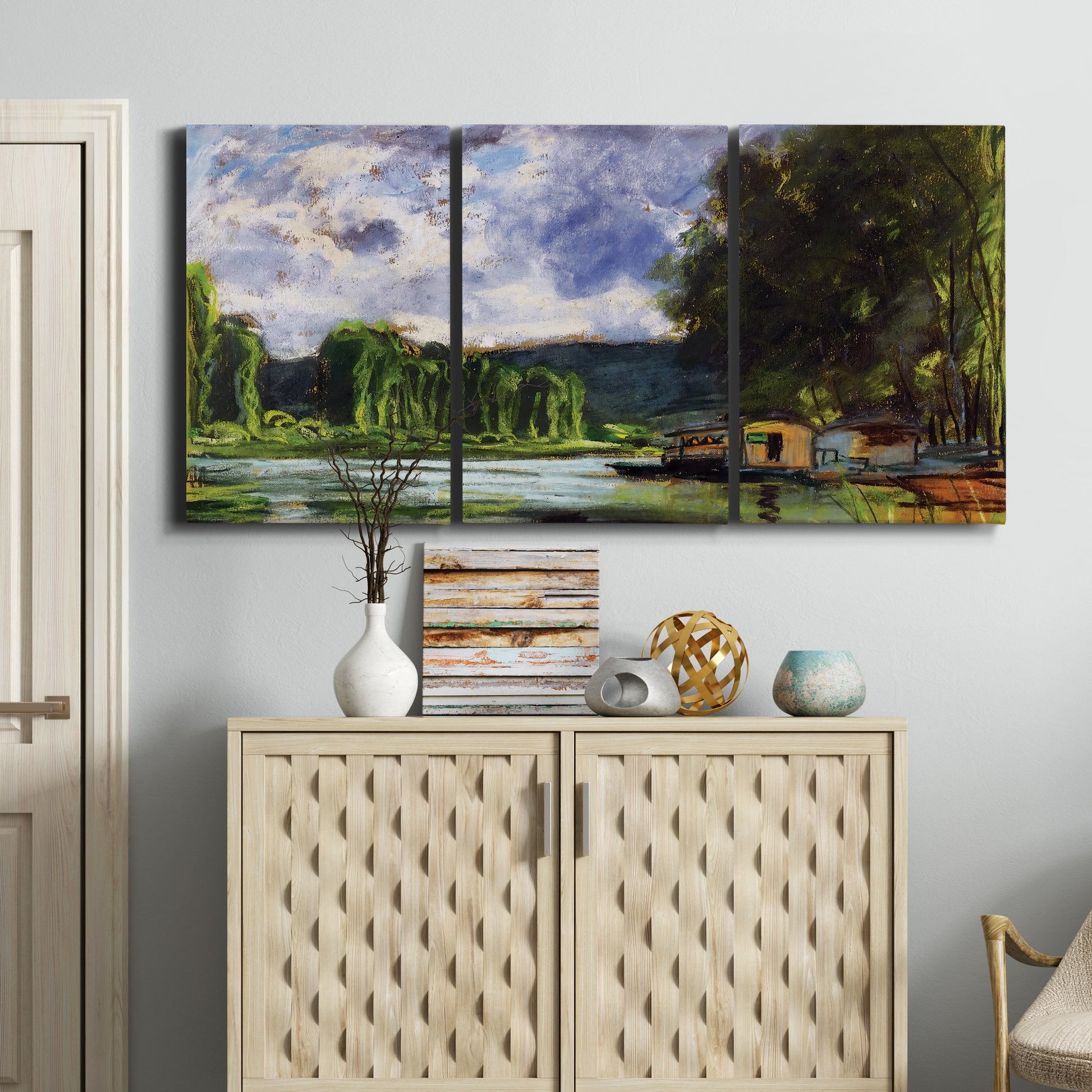 Three-panel canvas wall art featuring riverbank landscape near village, displayed above a cabinet in an entryway.