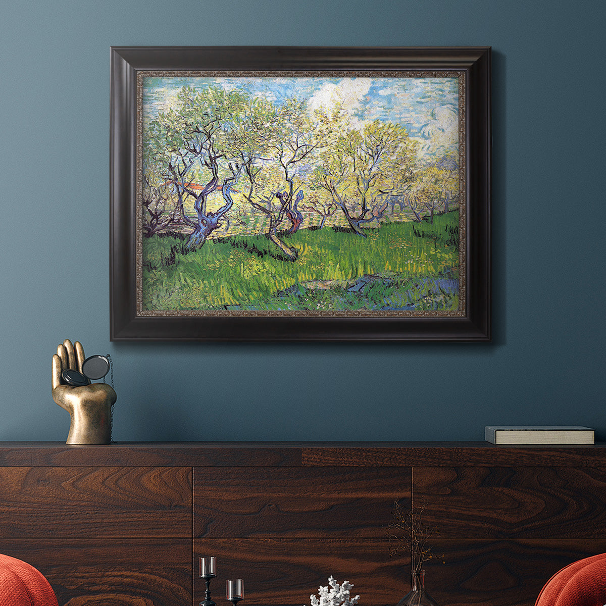 Impressionist spring orchard landscape by Vincent van Gogh in an ornate black frame with gilded inner detail displayed in a dark-toned interior setting.