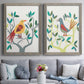 Set of two gray barnwood framed canvas prints depicting paired modern folk-art bird illustrations with red yellow blue plumage, simplified leaves, and playful flat shapes above a sofa in a contemporary living room.