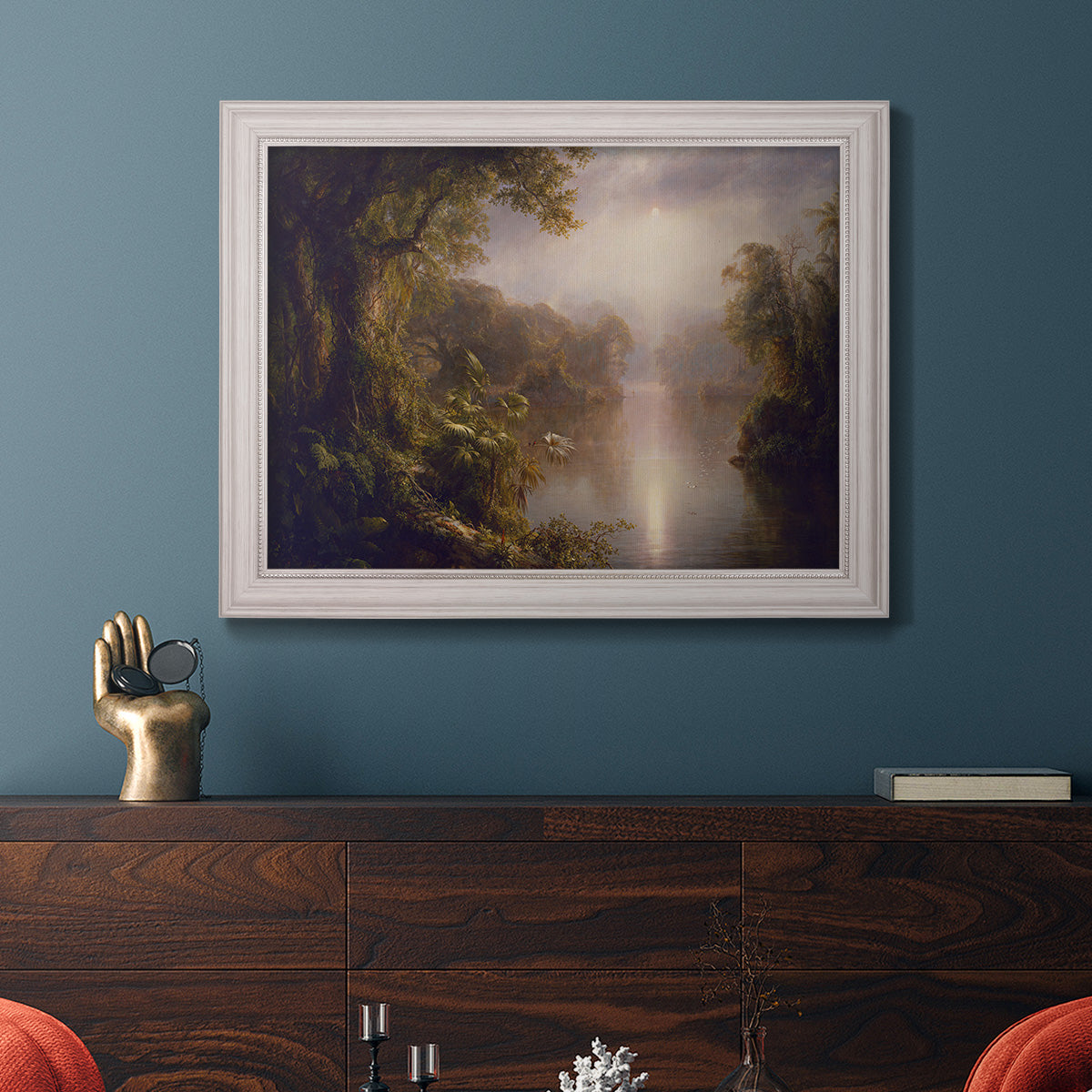 Luminous romantic landscape painting by Frederic Edwin Church in an ornate champagne frame displayed in a dark-toned interior setting.