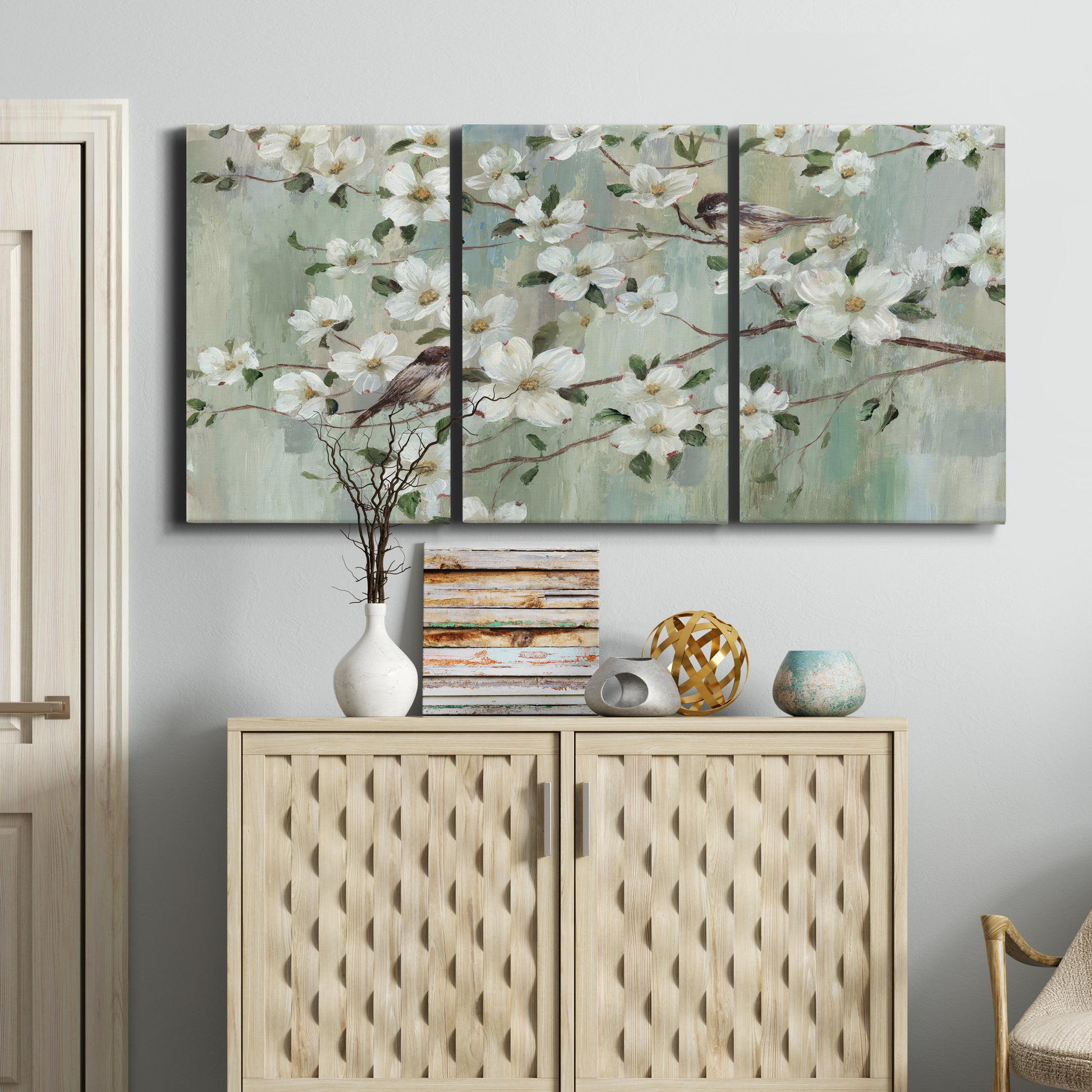 Three-panel canvas wall art featuring delicate spring blossoms with birds, displayed above a cabinet in an entryway.