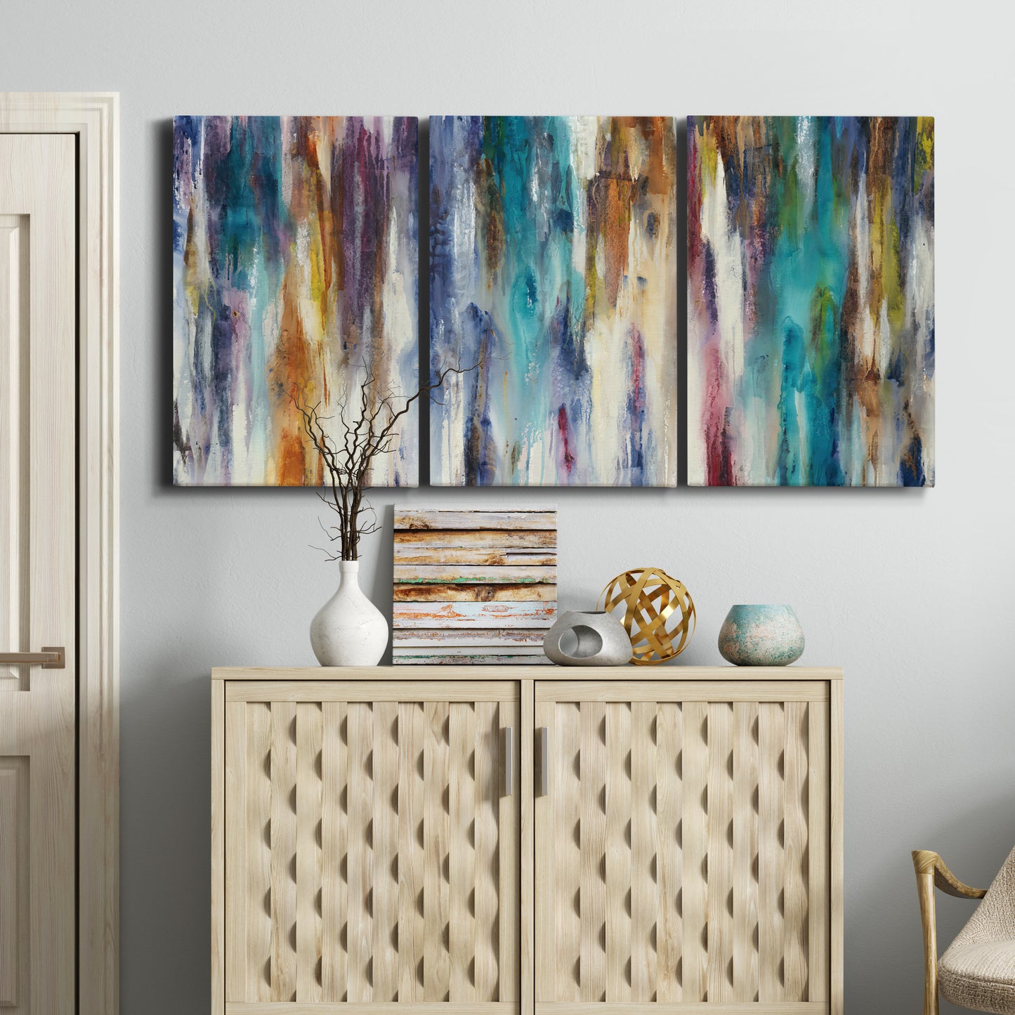 Three-panel canvas wall art featuring abstract shifting color forms, displayed above a cabinet in an entryway.