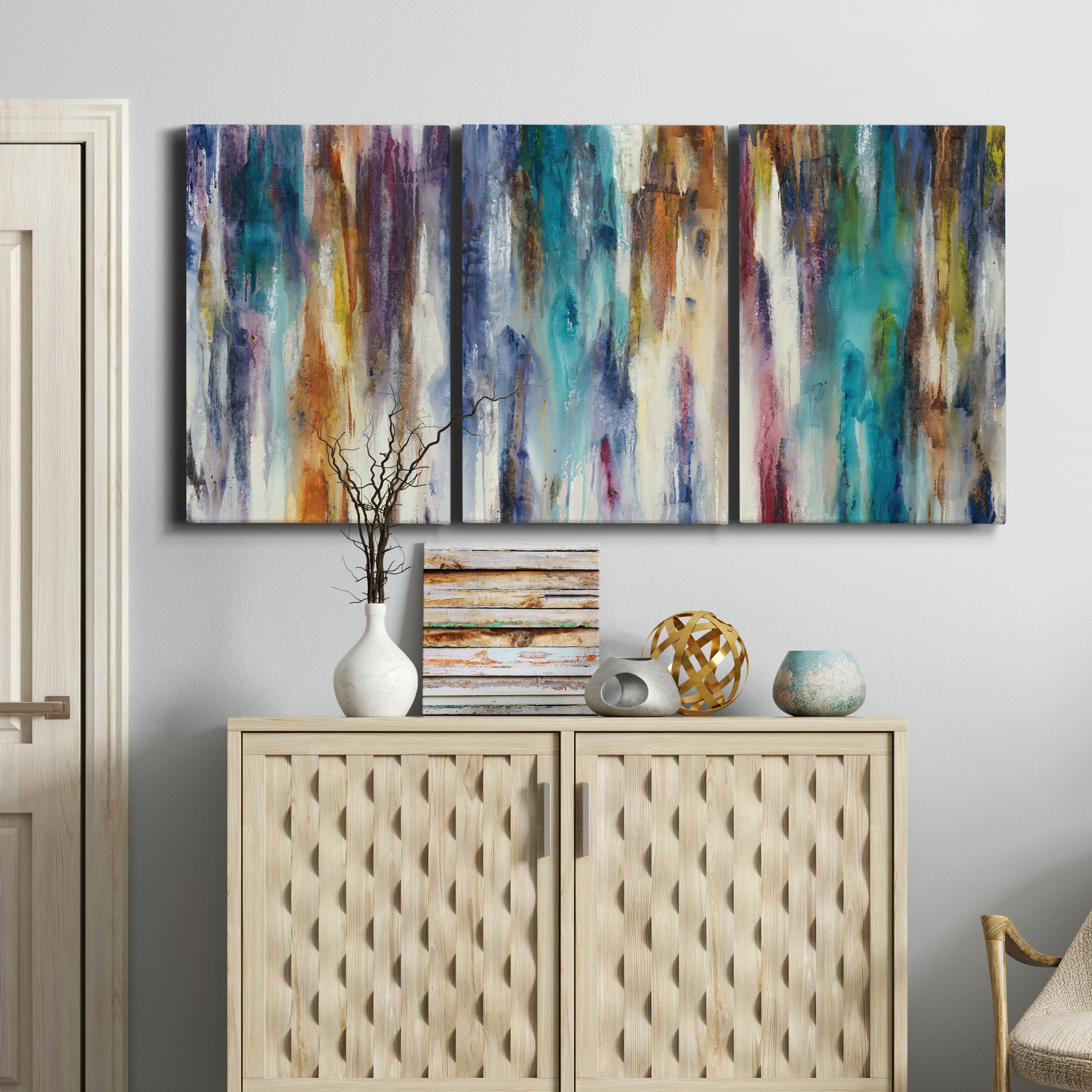 Three-panel canvas wall art featuring abstract shifting color forms, displayed above a cabinet in an entryway.