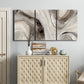 Three-panel canvas wall art featuring layered stone inspired abstract forms, displayed above a cabinet in an entryway.