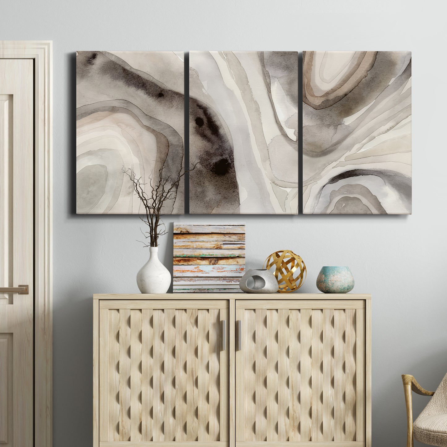 Three-panel canvas wall art featuring layered stone inspired abstract forms, displayed above a cabinet in an entryway.