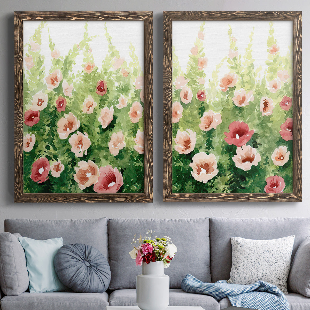 Set of two walnut barnwood framed canvas prints depicting paired luminous impressionistic floral paintings with loose blossoms, green stems, and sunlit watercolor texture above a sofa in a contemporary living room.