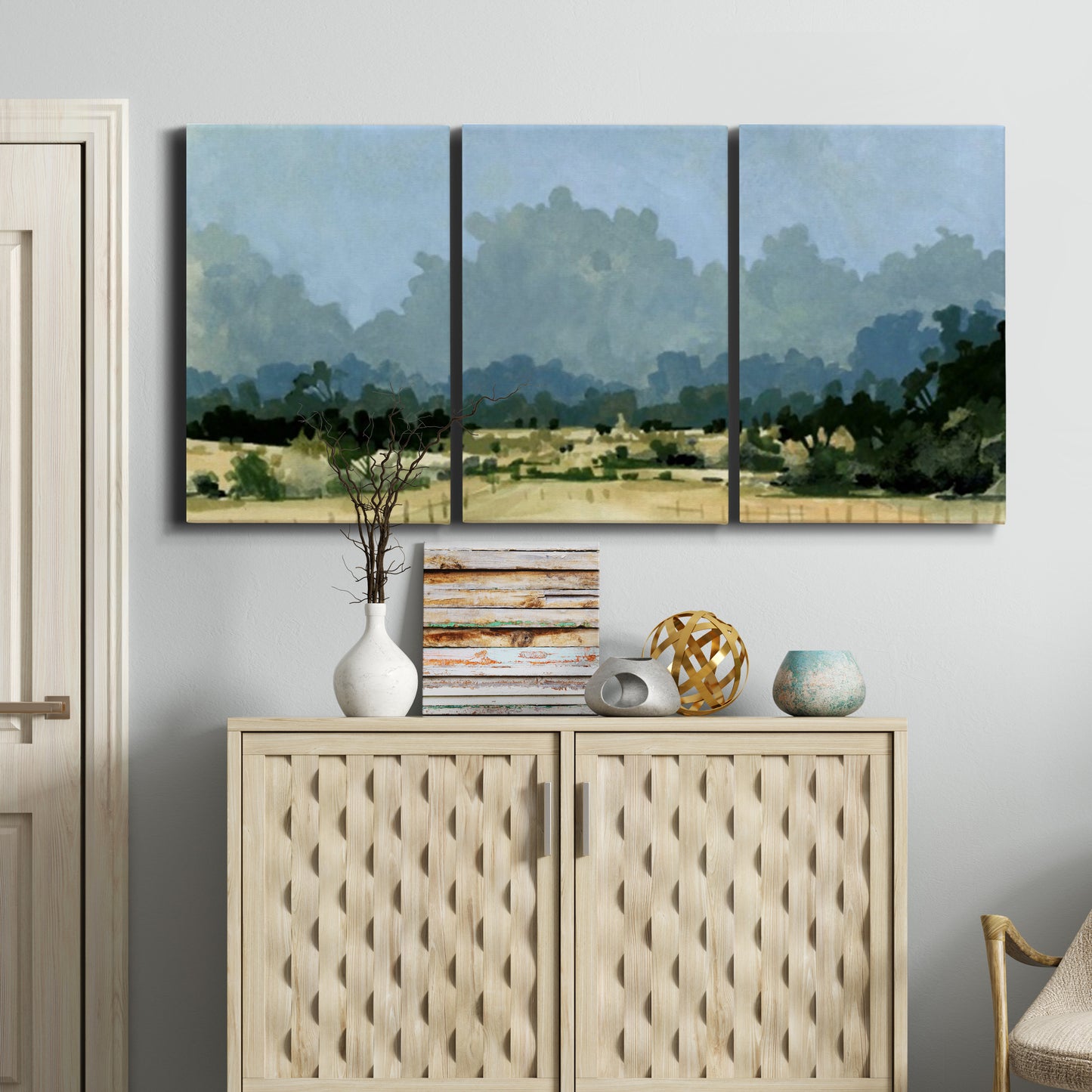 Three-panel canvas wall art featuring rural farmland landscape in watercolor, displayed above a cabinet in an entryway.