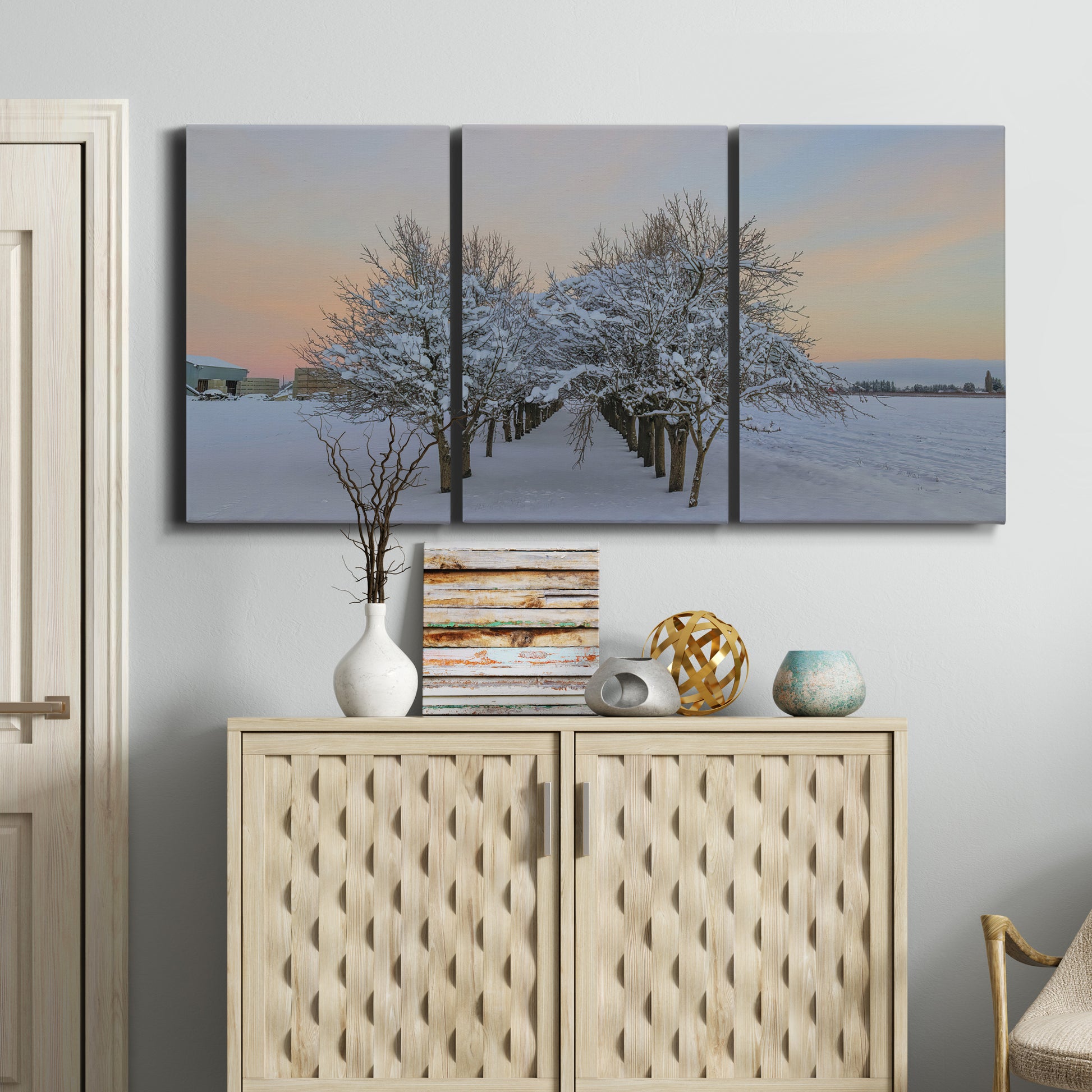 Three-panel canvas wall art featuring animals among snowy woodland trees, displayed above a cabinet in an entryway.