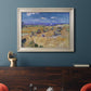 Impressionist wheat harvest scene by Vincent van Gogh in an ornate champagne frame displayed in a dark-toned interior setting.