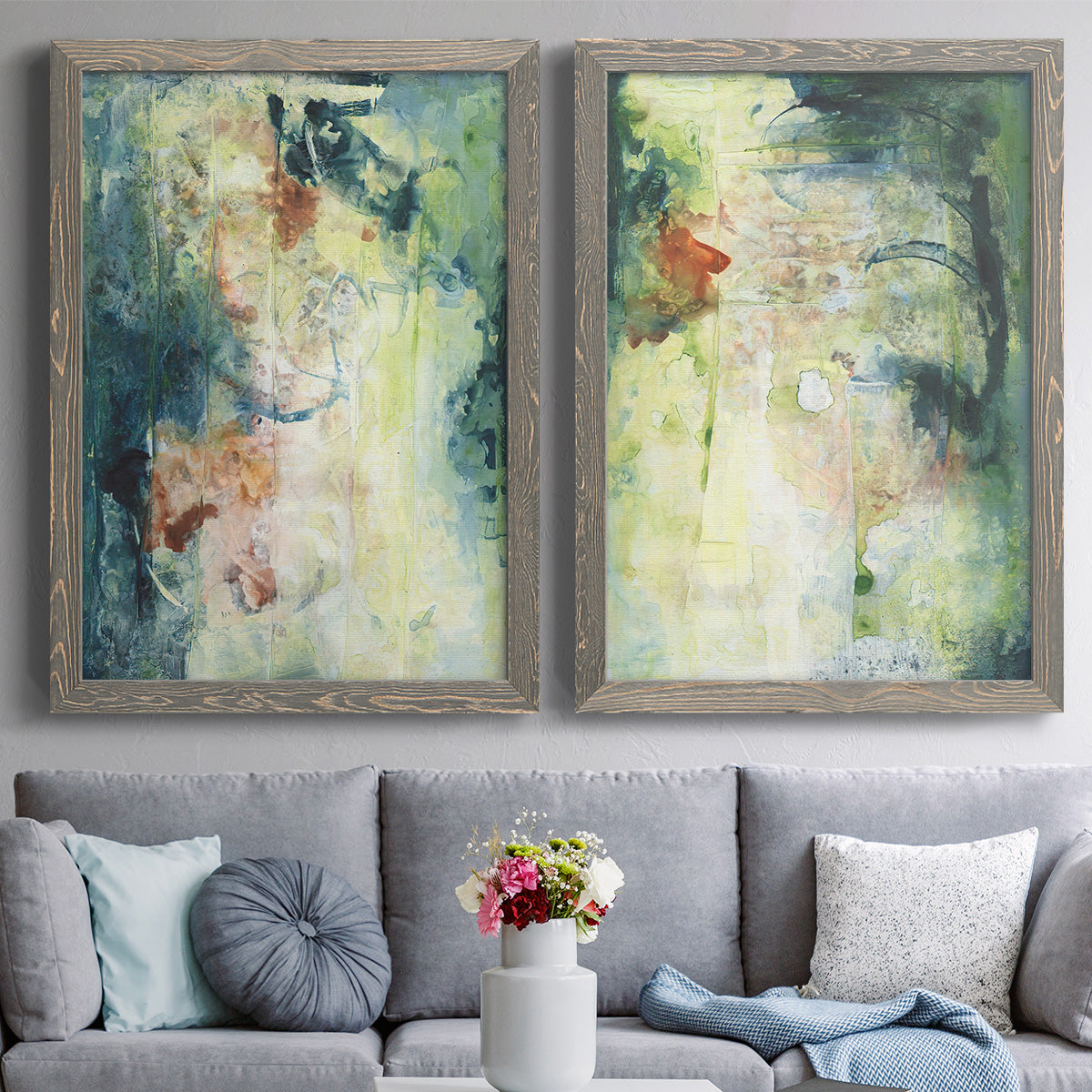 Set of two gray barnwood framed canvas prints depicting paired nature-inspired mixed-media abstracts with vertical organic marks, pale light passages, and weathered surfaces above a sofa in a contemporary living room.