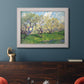 Impressionist spring orchard landscape by Vincent van Gogh in an ornate weathered white frame displayed in a dark-toned interior setting.