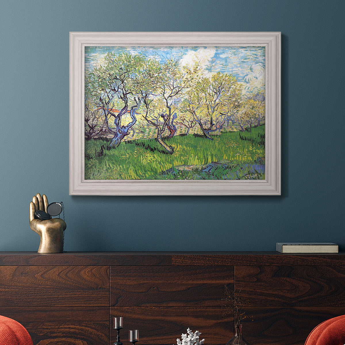 Impressionist spring orchard landscape by Vincent van Gogh in an ornate weathered white frame displayed in a dark-toned interior setting.