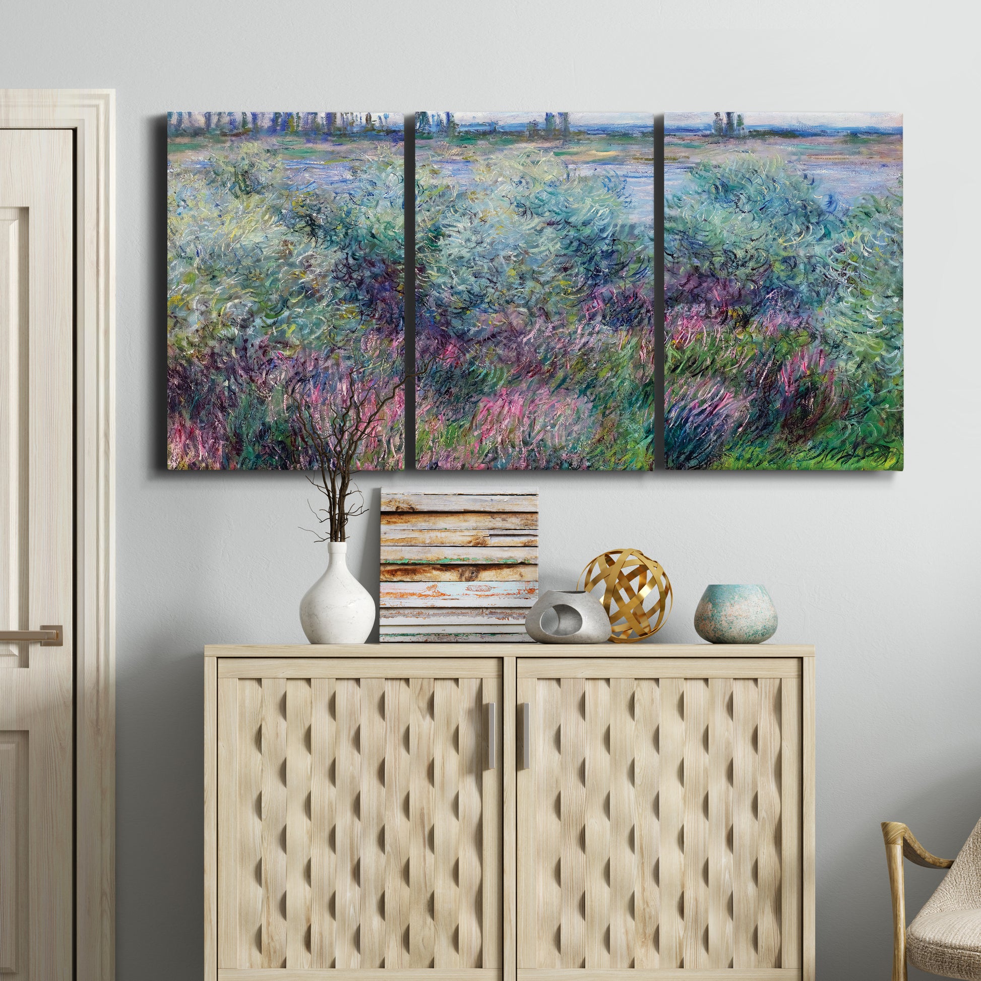 Three-panel canvas wall art featuring flowered riverbank with trees, displayed above a cabinet in an entryway.