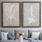 Set of two walnut barnwood framed canvas prints depicting paired rustic minimalist botanical prints with delicate stems, leaves, and blossoms against gray taupe and pale blue panels above a sofa in a contemporary living room.