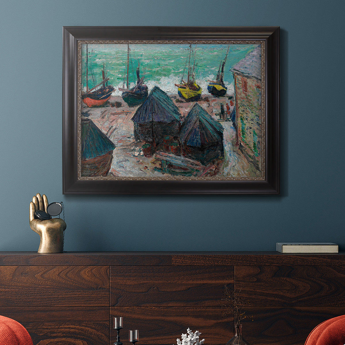 Impressionist coastal beach scene with boats by Claude Monet in an ornate black frame with gilded inner detail displayed in a dark-toned interior setting.