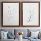 Set of two maple barnwood framed canvas prints depicting paired minimalist botanical line drawings with thin gray contours, sparse stems, and clean white fields above a sofa in a contemporary living room.