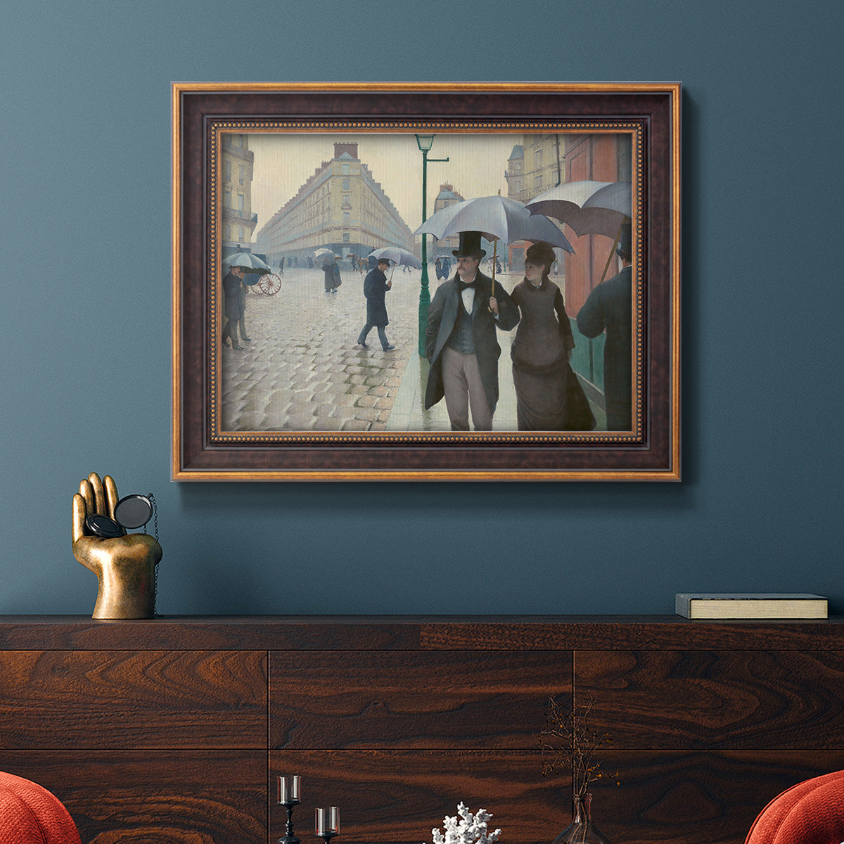 Impressionist urban street scene in the rain by Gustave Caillebotte in an ornate bronzed mahogany wood frame displayed in a dark-toned interior setting.