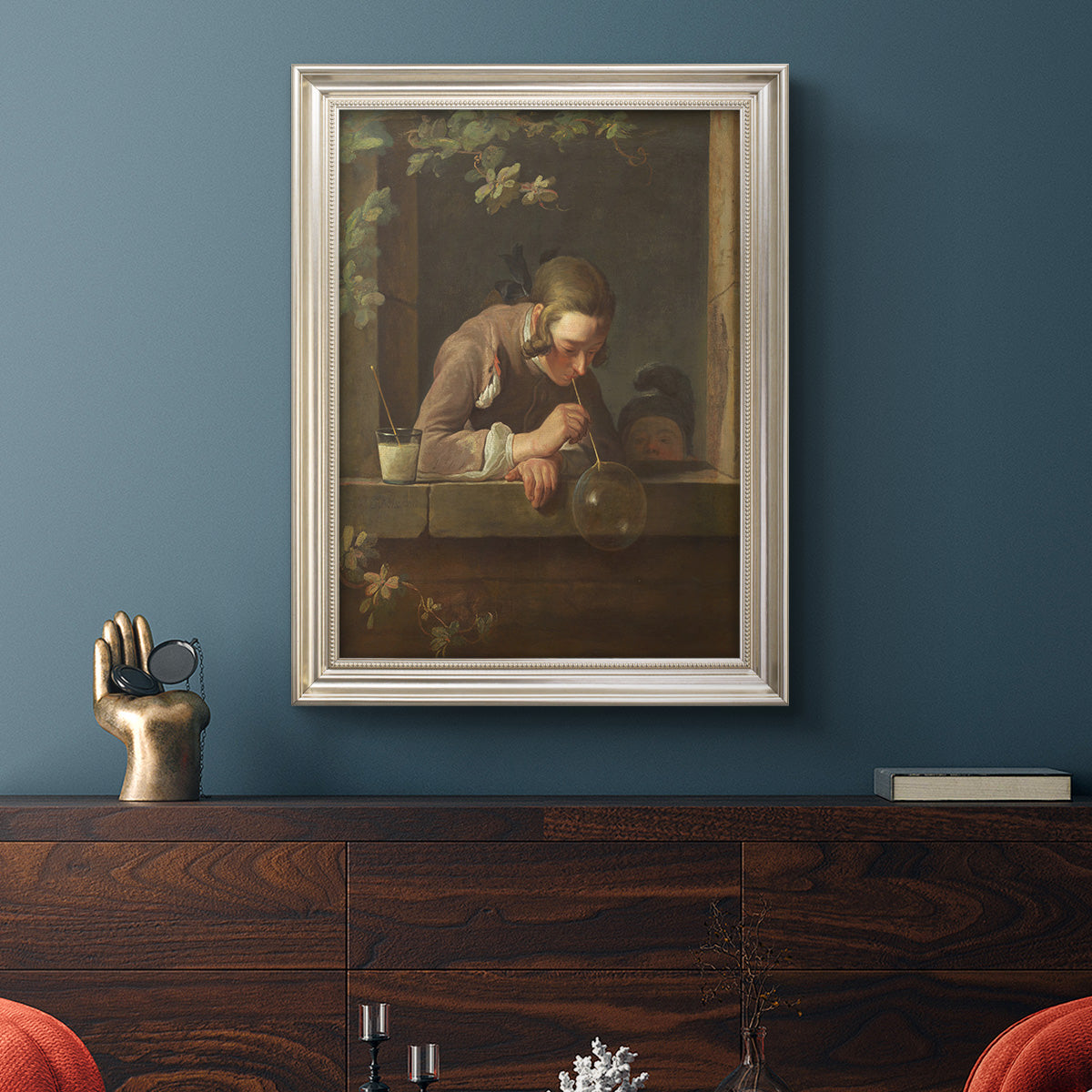 Classical genre painting of a child blowing soap bubbles by Jean-Siméon Chardin in an ornate champagne frame displayed in a dark-toned interior setting.