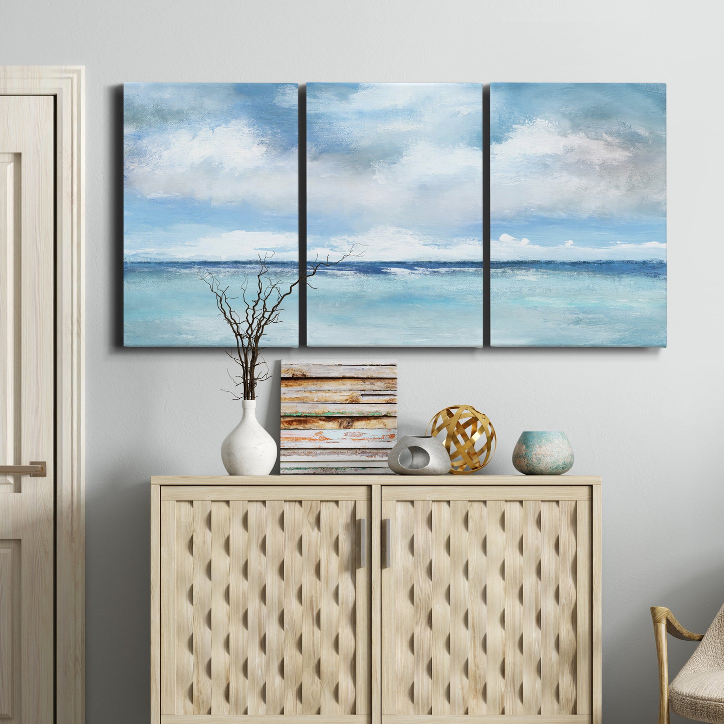 Three-panel canvas wall art featuring tropical clouds over ocean horizon, displayed above a cabinet in an entryway.