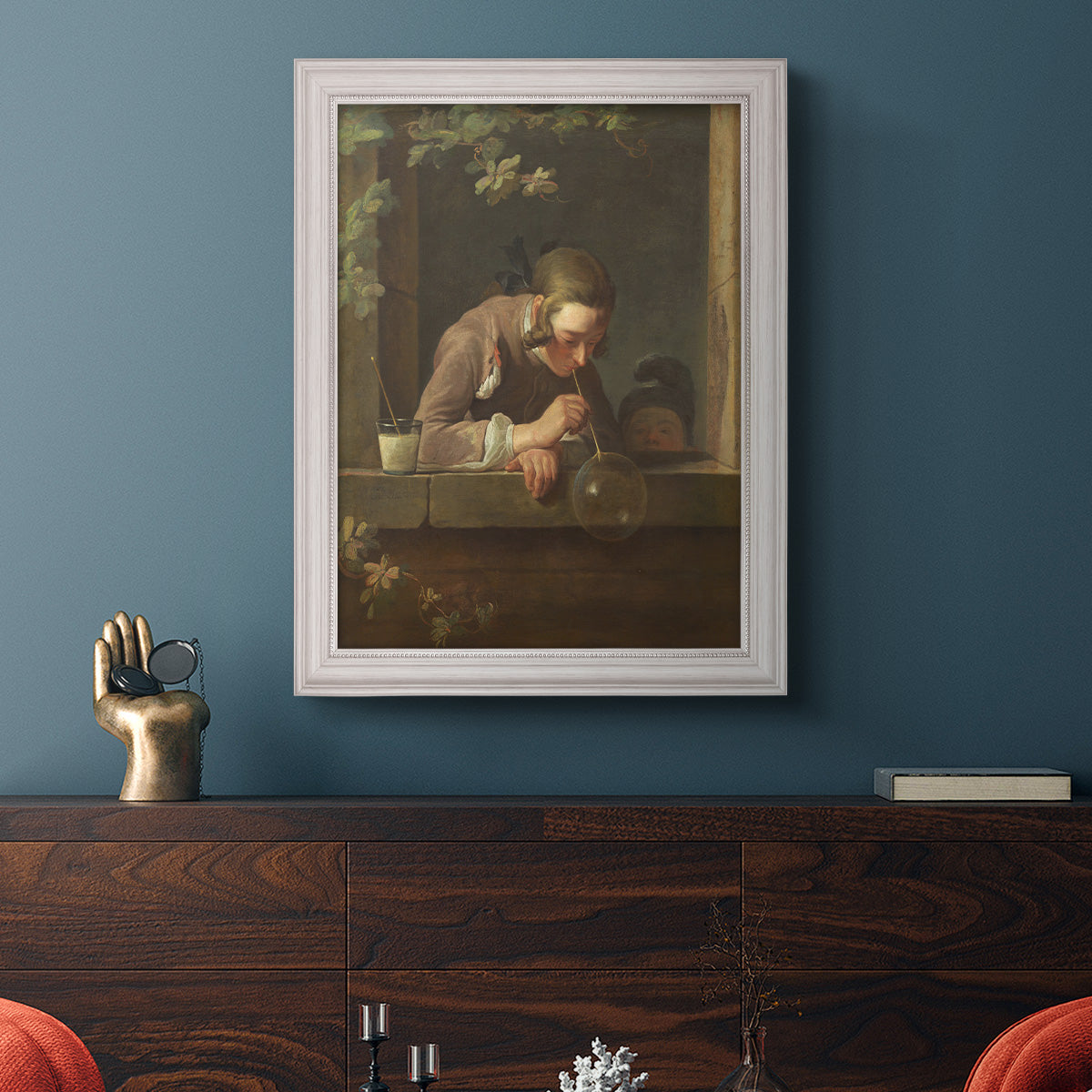 Classical genre painting of a child blowing soap bubbles by Jean-Siméon Chardin in an ornate weathered white frame displayed in a dark-toned interior setting.