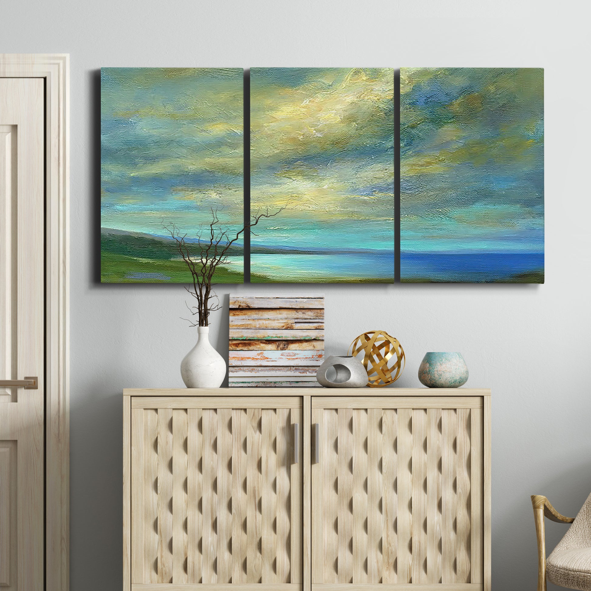 Three-panel canvas wall art featuring coastal shoreline with soft waves, displayed above a cabinet in an entryway.