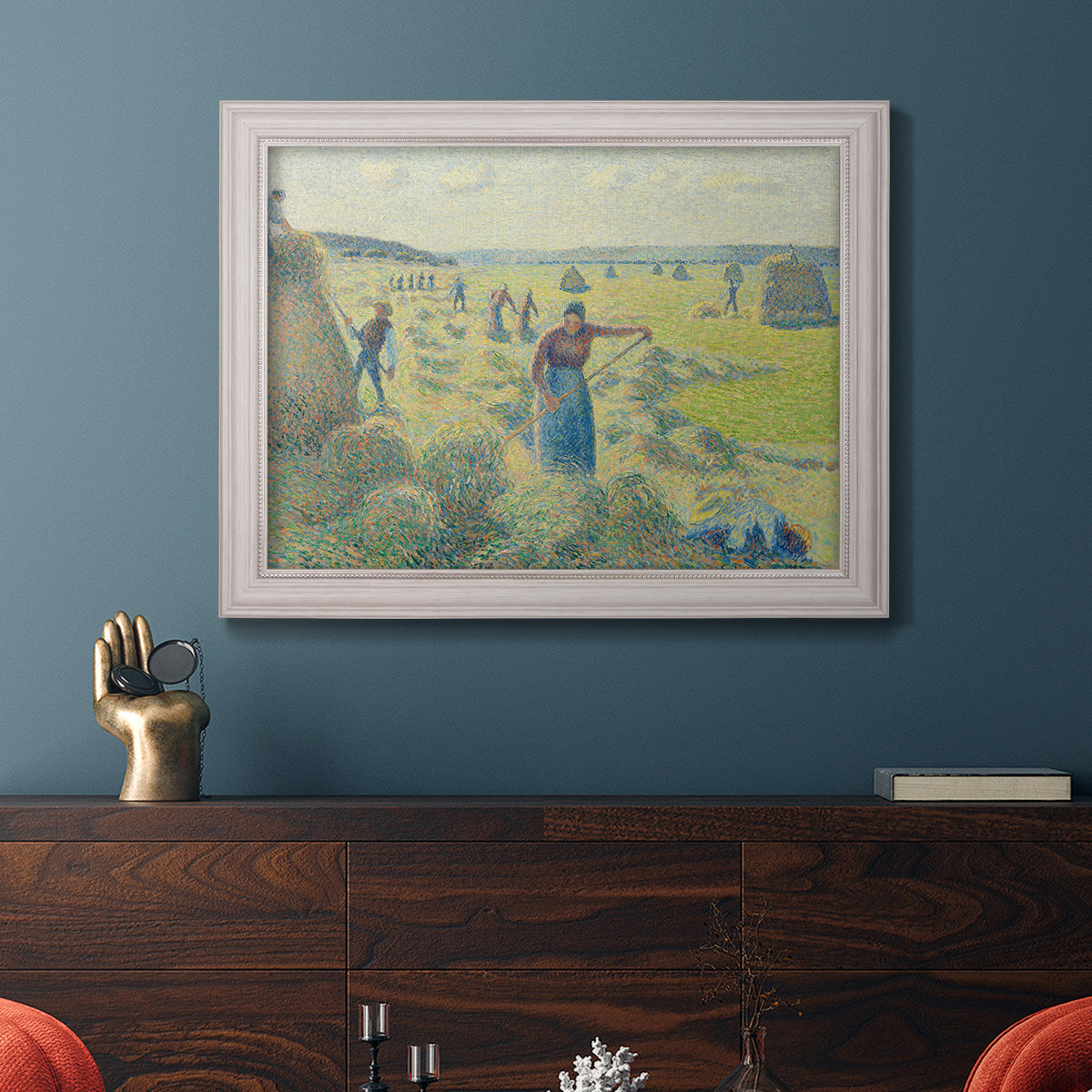 Impressionist rural hay harvest landscape by Camille Pissarro in an ornate weathered white frame displayed in a dark-toned interior setting.