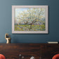 Impressionist white-blossomed orchard landscape by Vincent van Gogh in an ornate weathered white frame displayed in a dark-toned interior setting.