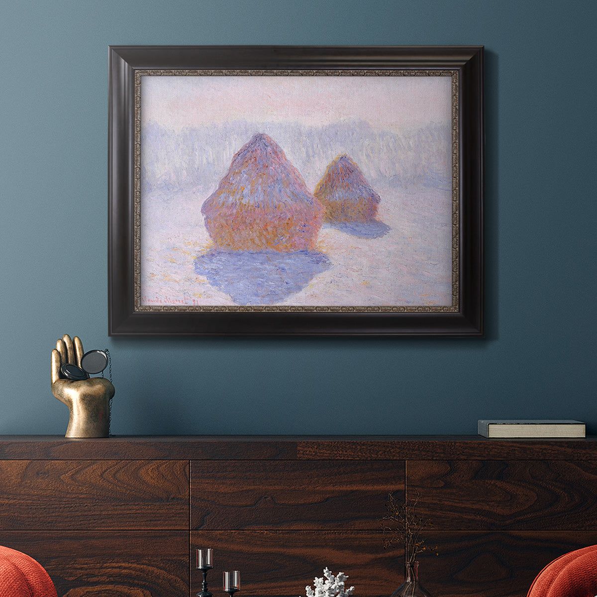 Impressionist winter haystack scene with sunlight by Claude Monet in an ornate black frame with gilded inner detail displayed in a dark-toned interior setting.