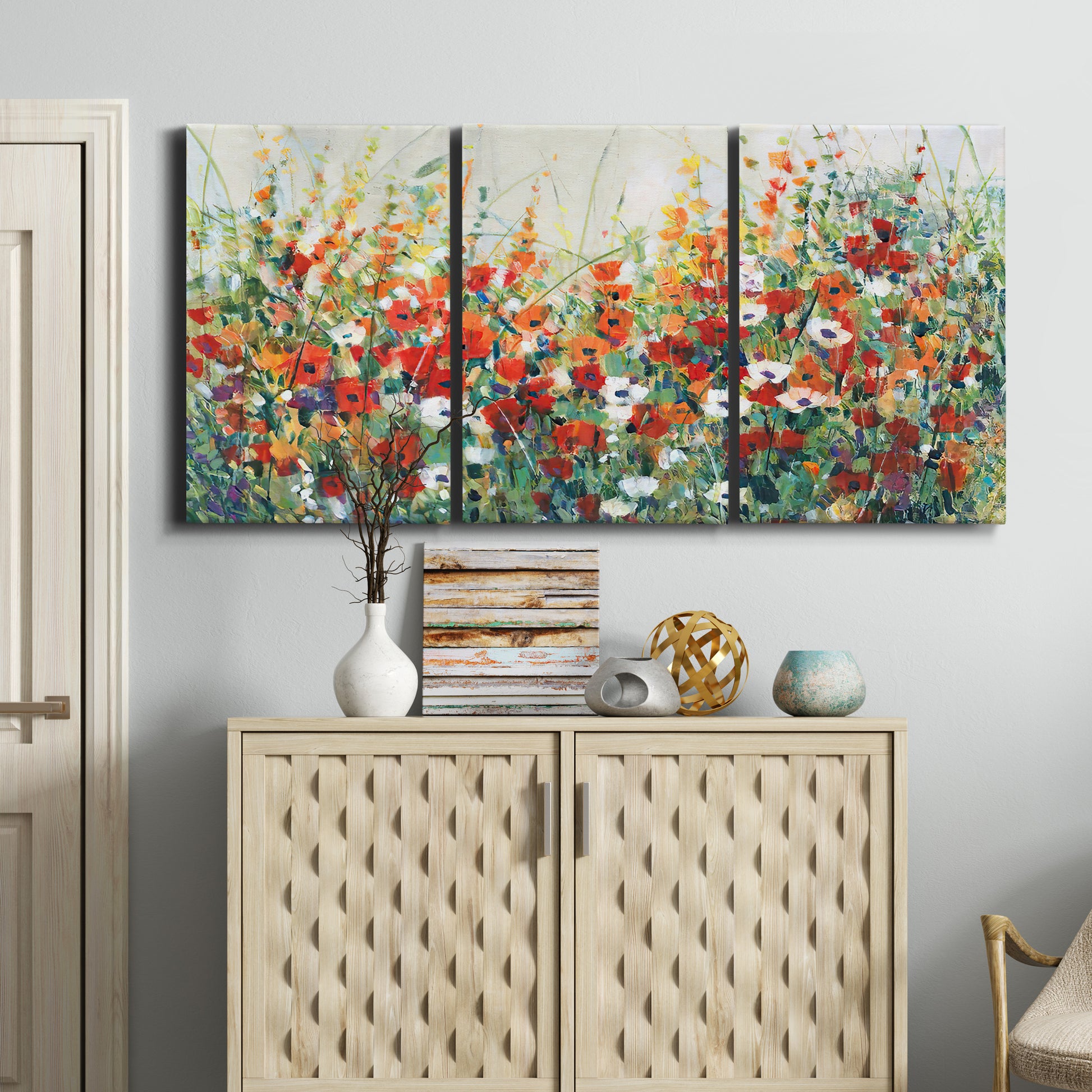 Three-panel canvas wall art featuring colorful garden flowers in bloom, displayed above a cabinet in an entryway.
