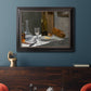 Impressionist still life with wine and bread by Claude Monet in an ornate black frame with gilded inner detail displayed in a dark-toned interior setting.