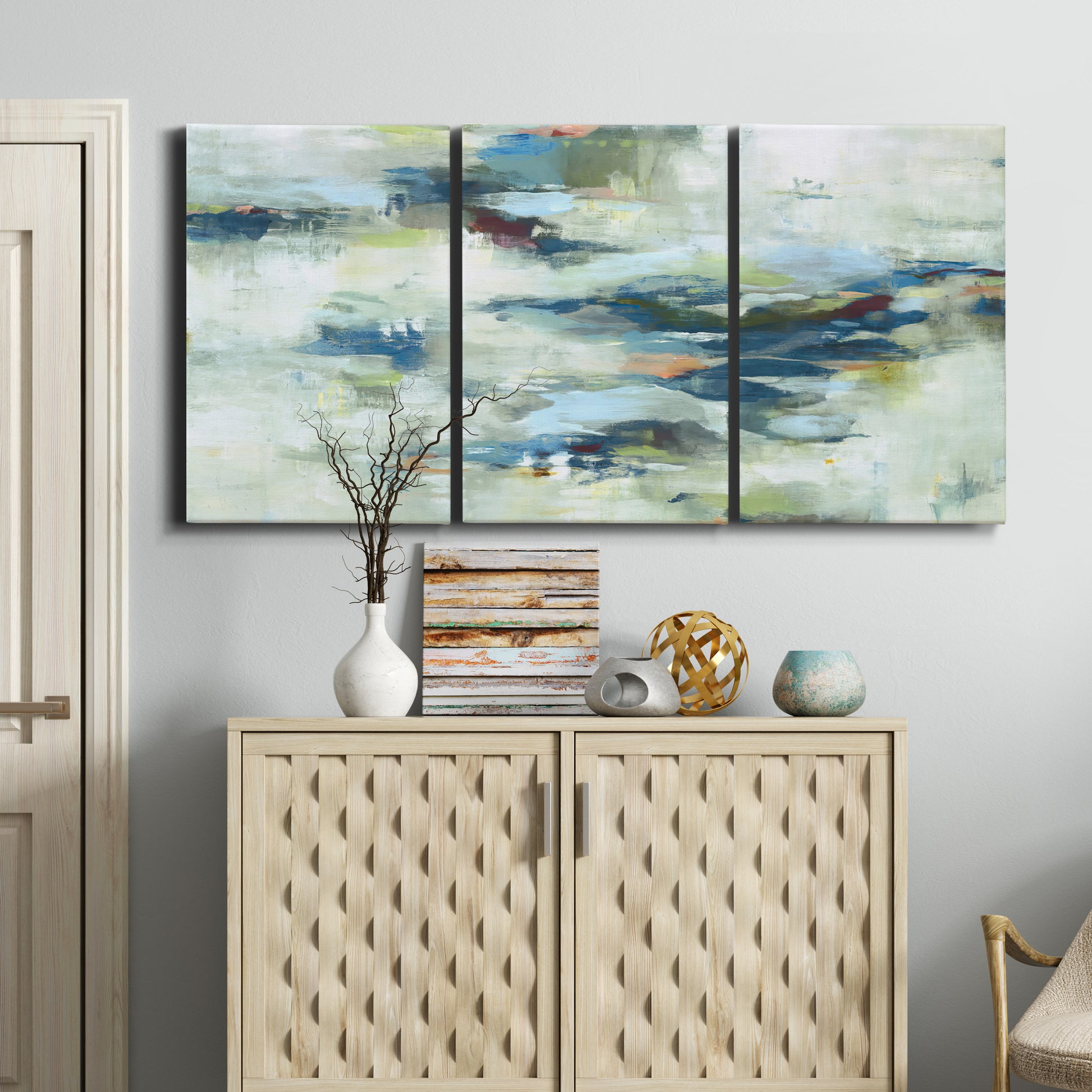 Three-panel canvas wall art featuring dreamlike abstract drifting motion, displayed above a cabinet in an entryway.