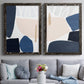 Set of two black barnwood framed canvas prints depicting paired minimalist color-block abstracts with rounded dark forms, pale sand fields, and clean modern edges above a sofa in a contemporary living room.