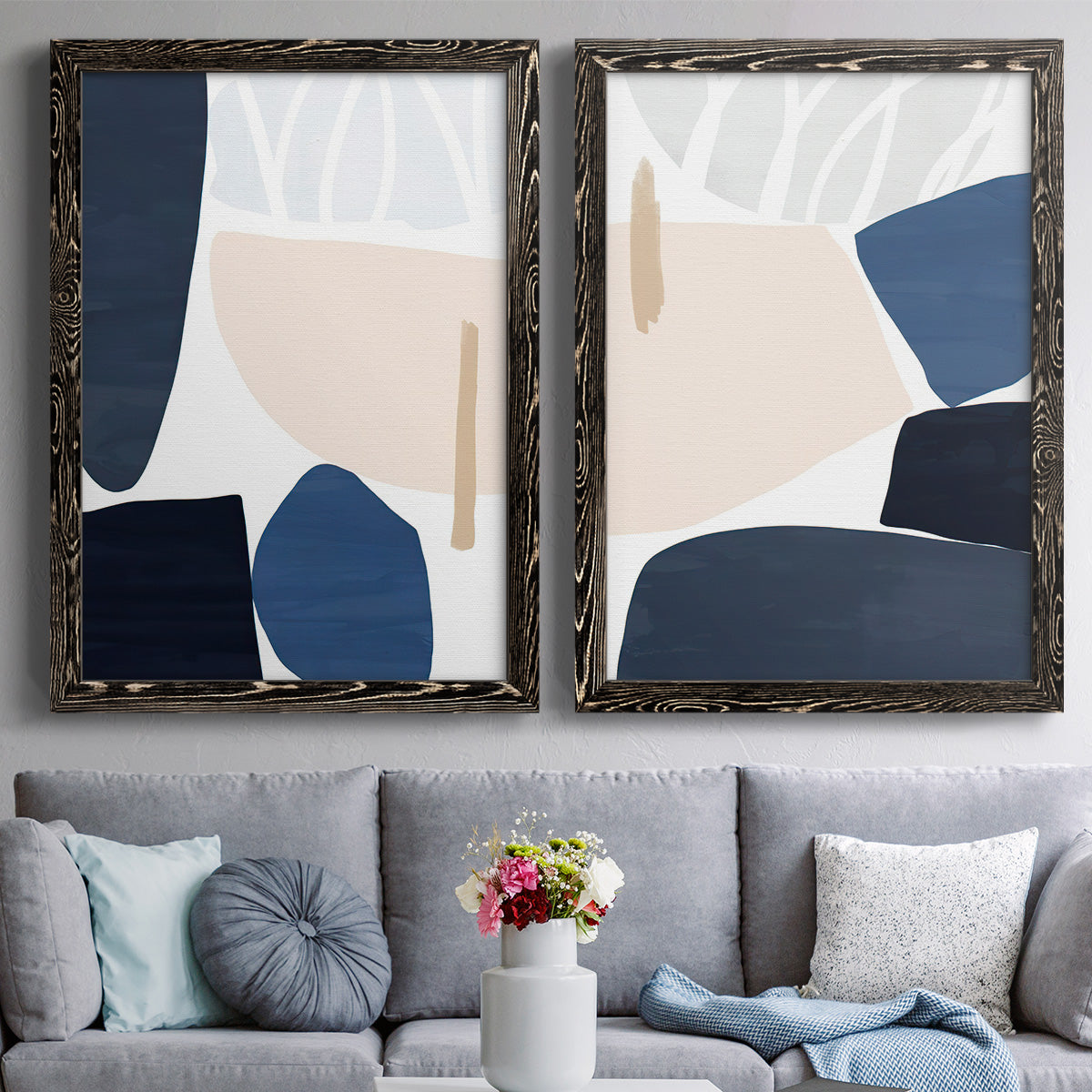 Set of two black barnwood framed canvas prints depicting paired minimalist color-block abstracts with rounded dark forms, pale sand fields, and clean modern edges above a sofa in a contemporary living room.