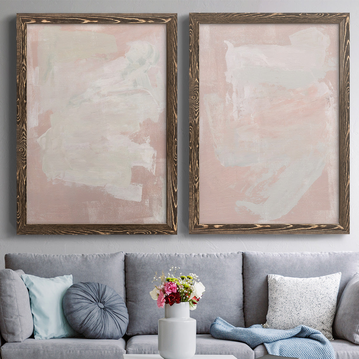 Set of two walnut barnwood framed canvas prints depicting paired minimalist color-field abstracts with cloudy rose washes, broad pale strokes, and subtle texture above a sofa in a contemporary living room.