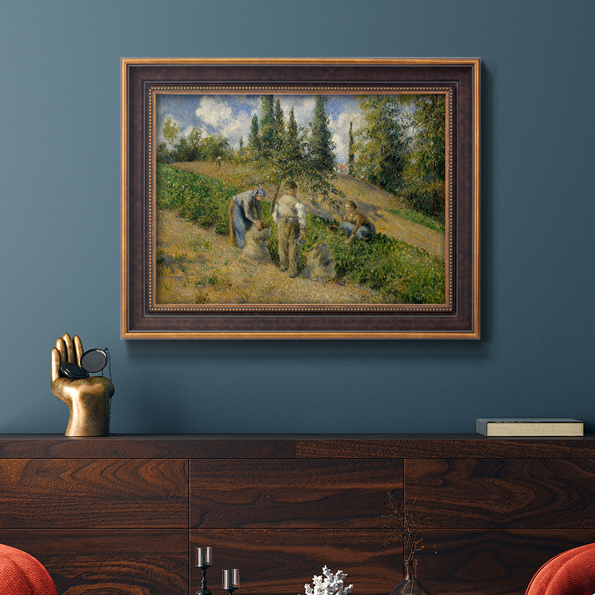 Impressionist countryside harvest scene by Camille Pissarro in an ornate bronzed mahogany wood frame displayed in a dark-toned interior setting.
