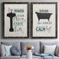Set of two black barnwood framed canvas prints depicting paired graphic bathroom word art with black tubs, hand-lettered phrases, and small teal accents above a sofa in a contemporary living room.