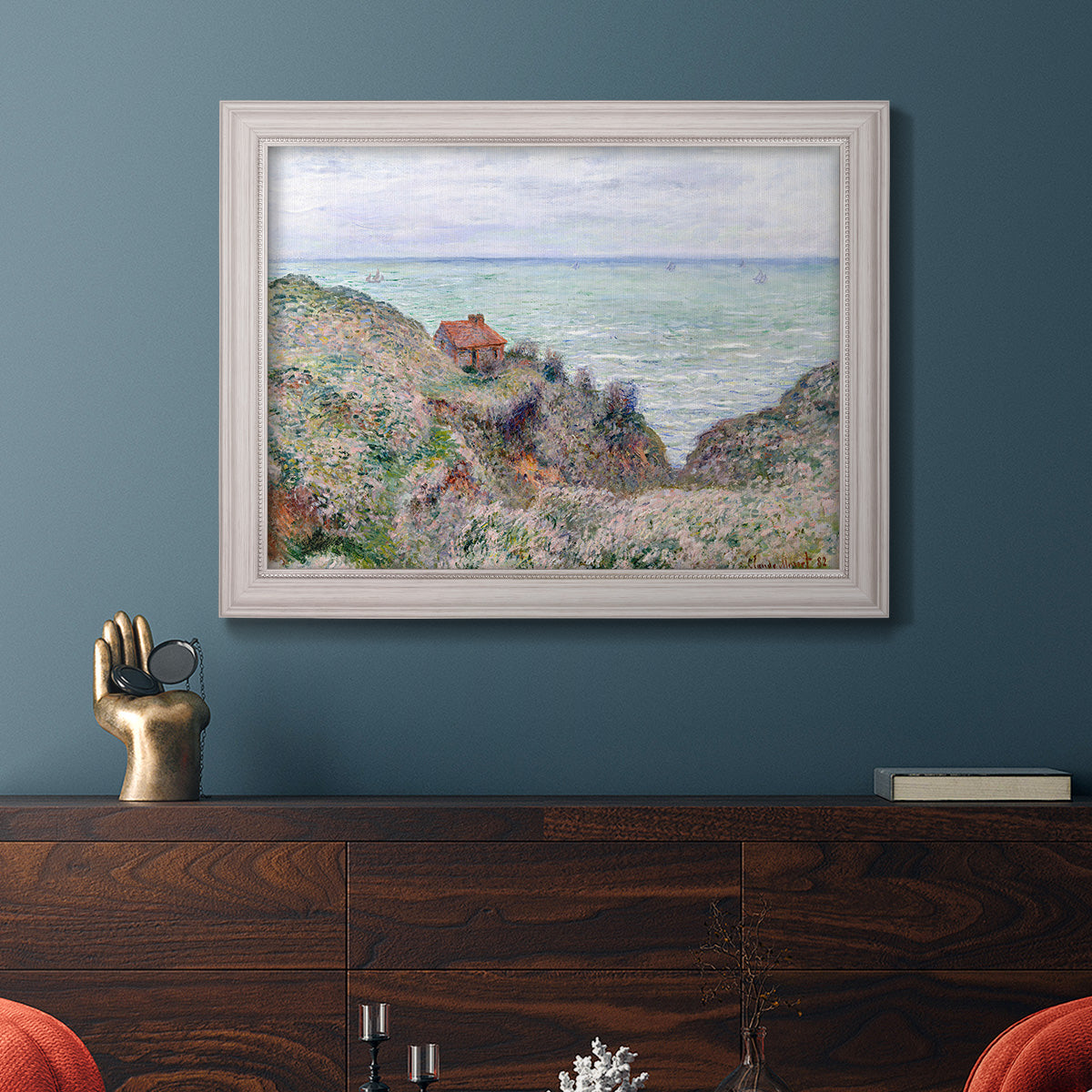 Impressionist coastal watch cabin scene by Claude Monet in an ornate weathered white frame displayed in a dark-toned interior setting.