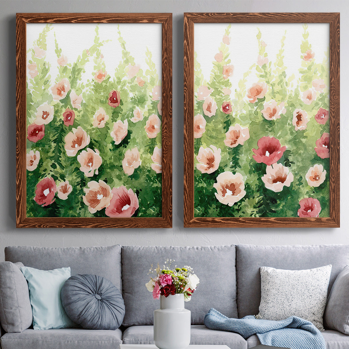 Set of two maple barnwood framed canvas prints depicting paired luminous impressionistic floral paintings with loose blossoms, green stems, and sunlit watercolor texture above a sofa in a contemporary living room.