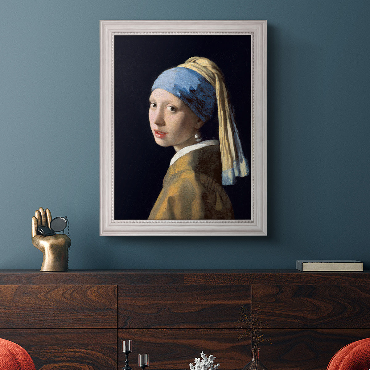 Iconic portrait of a girl wearing a pearl earring by Johannes Vermeer in an ornate weathered white frame displayed in a dark-toned interior setting.