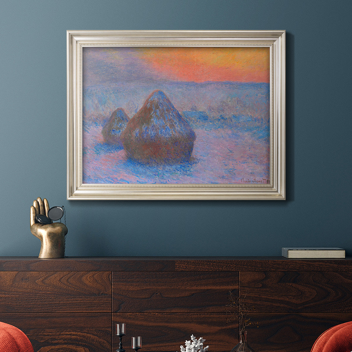 Impressionist haystack scene at sunset by Claude Monet in an ornate champagne frame displayed in a dark-toned interior setting.