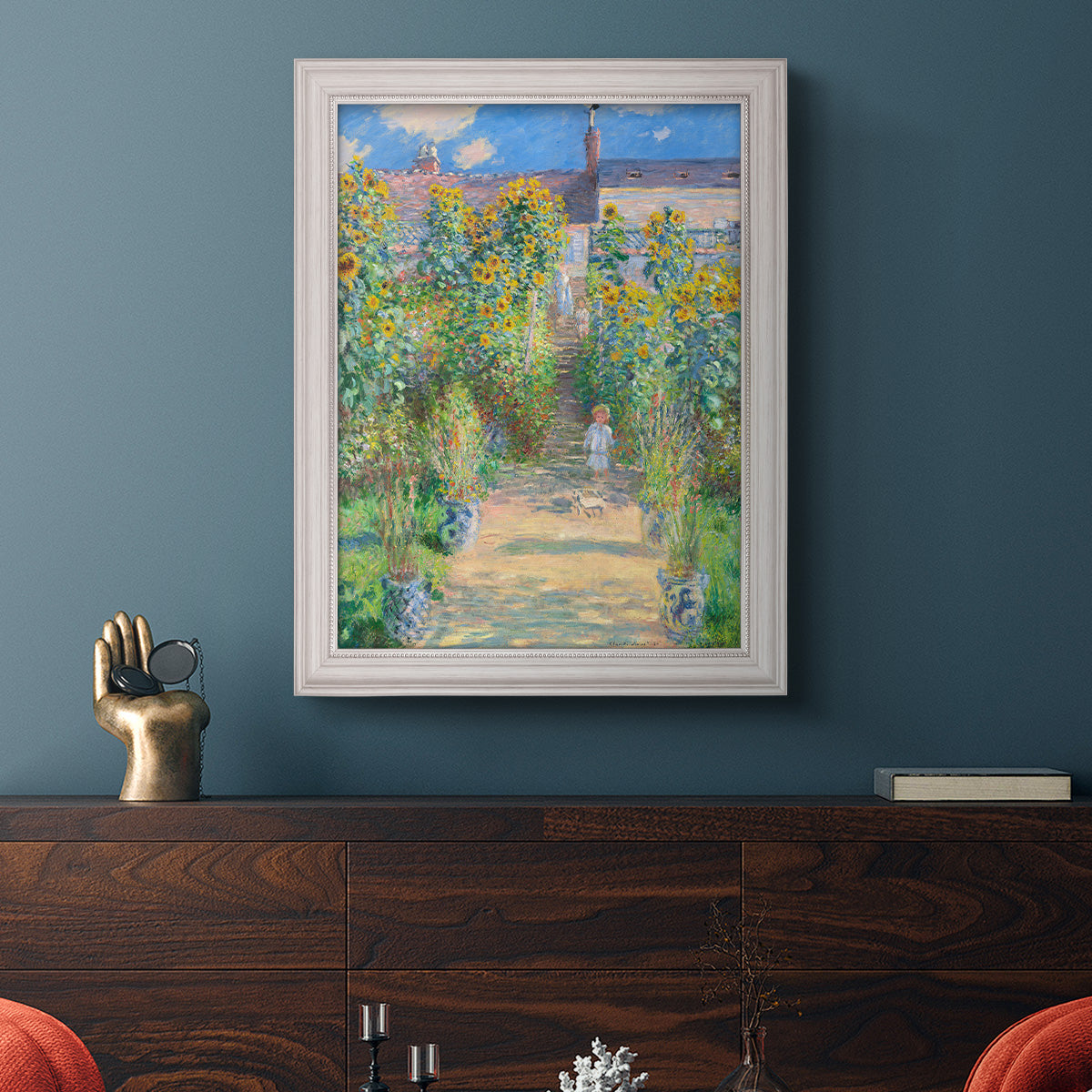 Impressionist garden landscape painting by Claude Monet in an ornate weathered white frame displayed in a dark-toned interior setting.