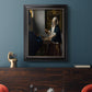 Quiet interior genre scene of a woman with scales by Johannes Vermeer in an ornate black frame with gilded inner detail displayed in a dark-toned interior setting.