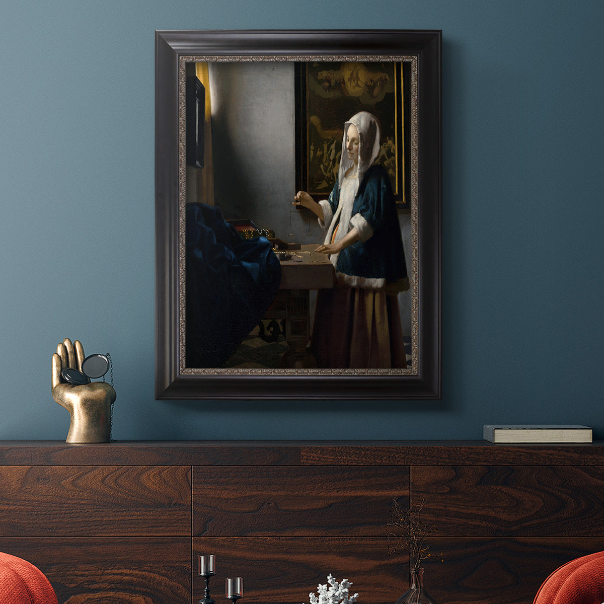 Quiet interior genre scene of a woman with scales by Johannes Vermeer in an ornate black frame with gilded inner detail displayed in a dark-toned interior setting.
